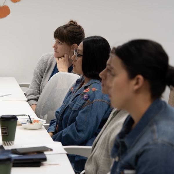 Three people seated at a conference table, listening attentively during a meeting or workshop.