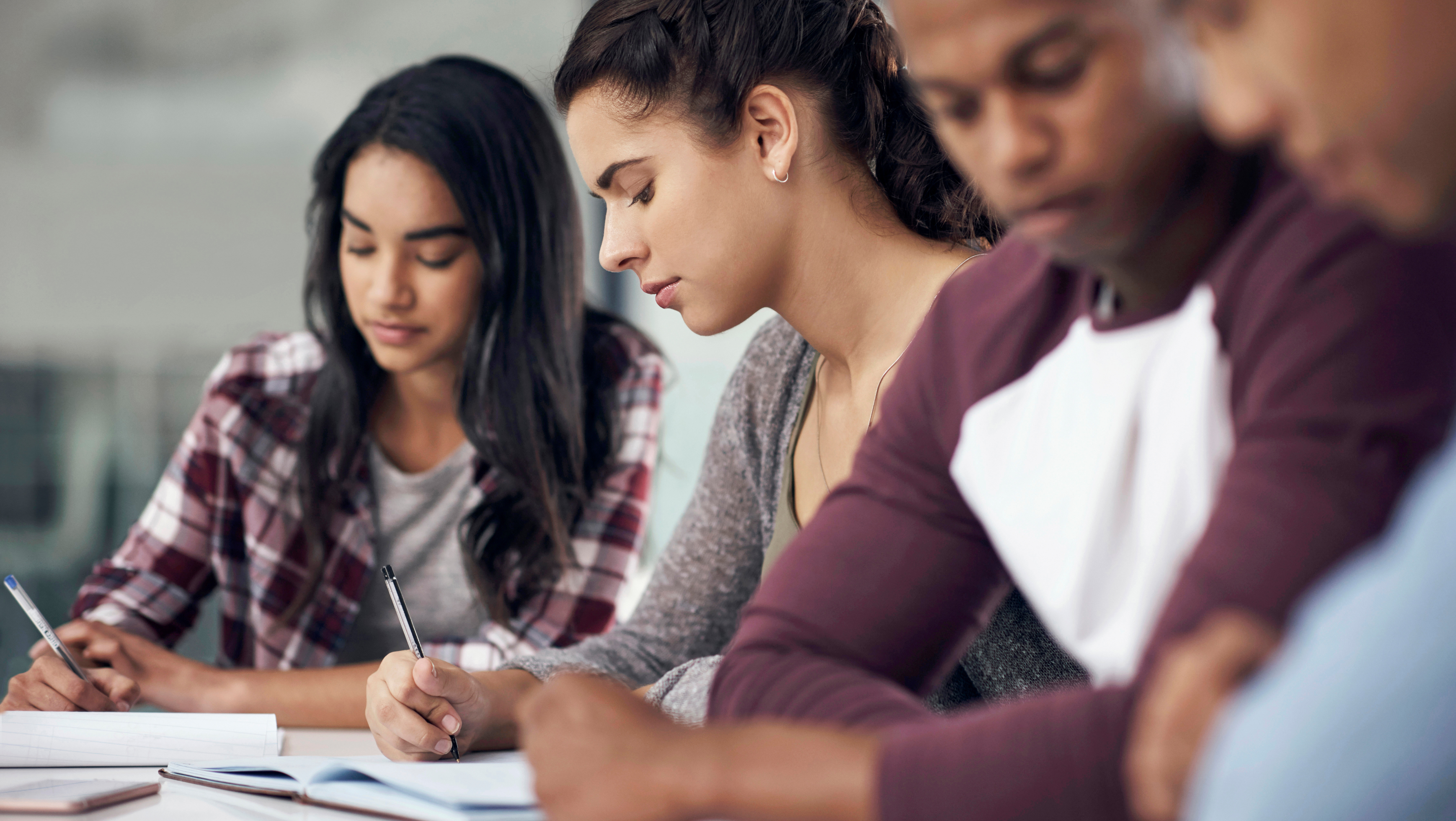 Three students sitting side by side and writing in notebooks during a study session.